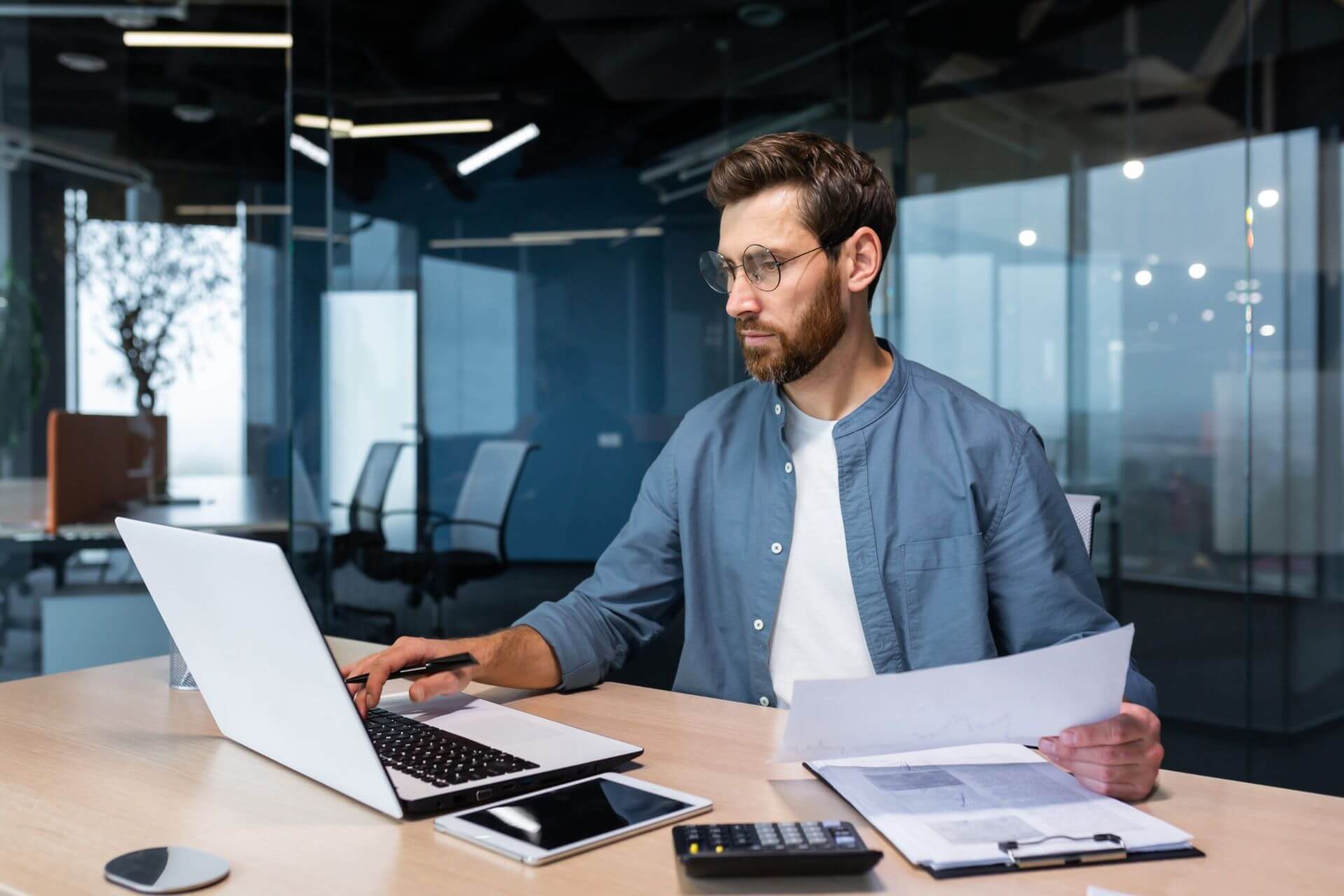 A Person in a Blue Shirt Sitting at a Modern Office Desk Working on a Laptop