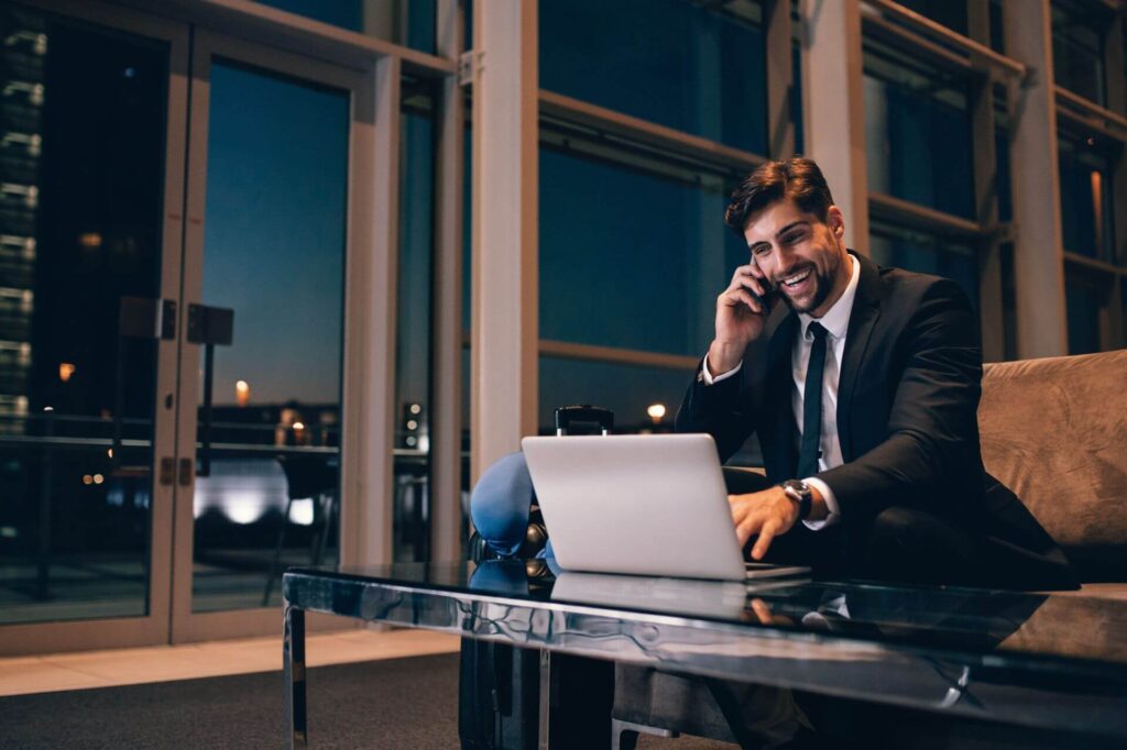 Man in Suit on Couch, Using Laptop and Phone, Satisfied With IT Services