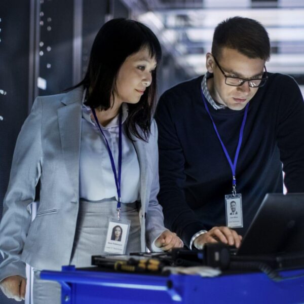 Two IT Professionals, a Man, and a Woman Collaborating on a Laptop in a Server Room